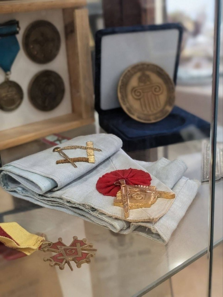 Vitrina con bandas masónicas bordadas, collares y joyas distintivas de la logia